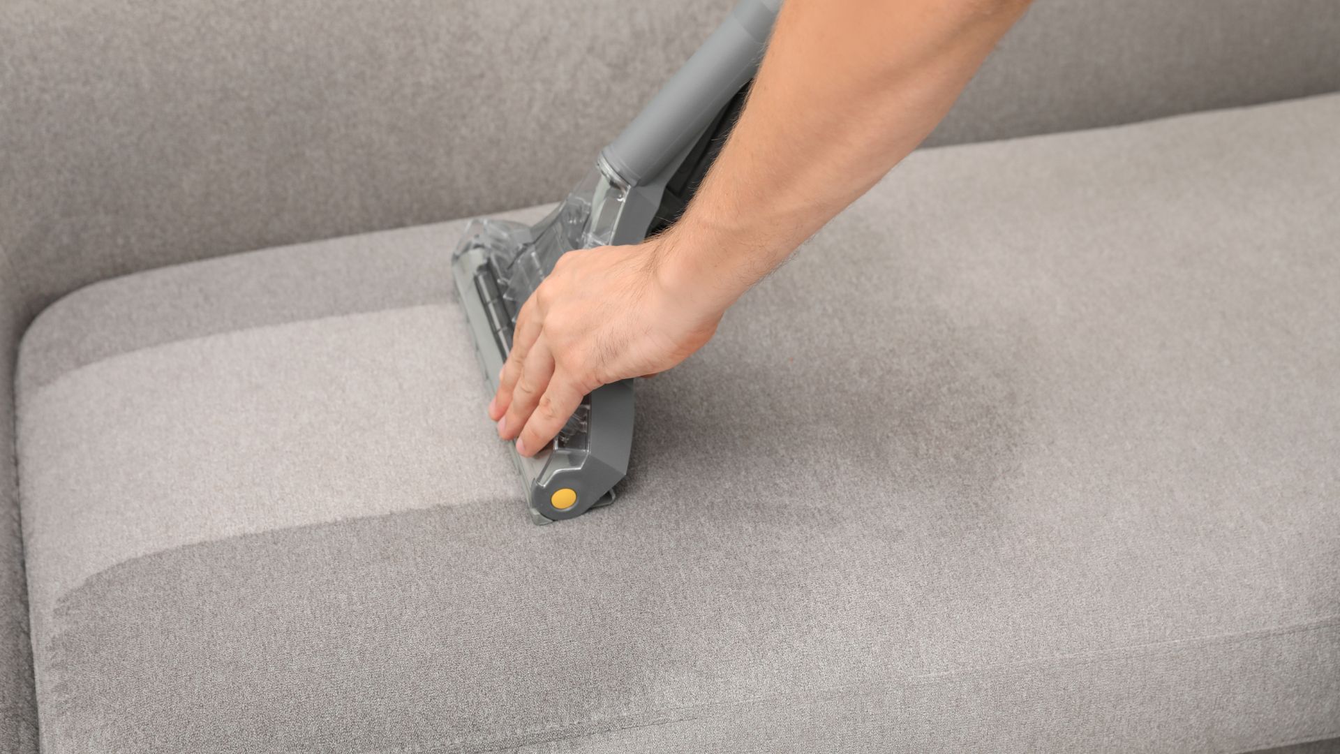 A person using a vacuum to clean a couch